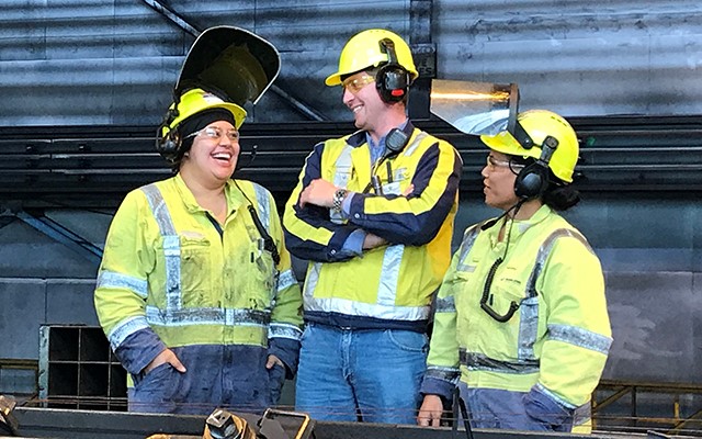 Three workers in high-vis gear and safety helmets working in production plant
