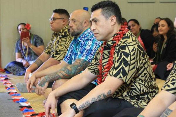 Pacific men sit cross legged on the floor at work conference