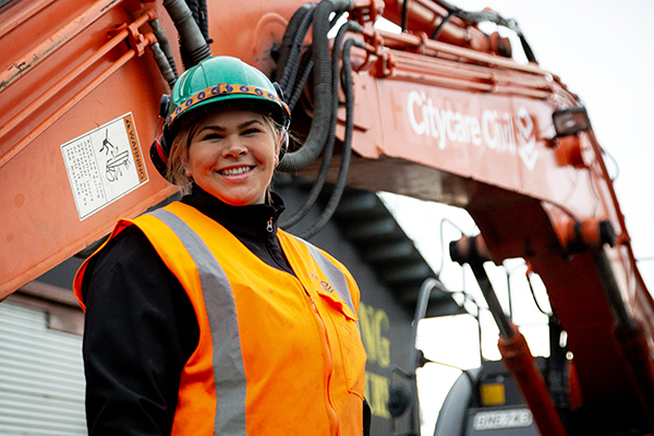 Woman in high-vis and hard hat in front of digger
