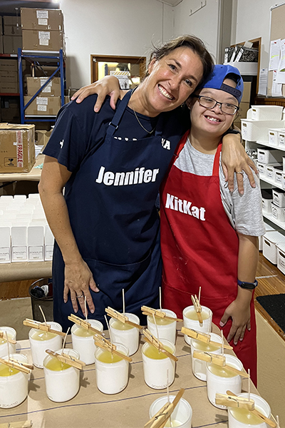 Candle-makers, one with down syndrome, arm-in-arm behind candles in progress
