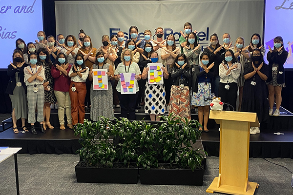 Women standing on stage in face masks, doing 'break the bias' pose