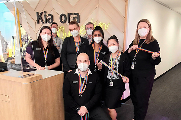 Bank workers wearing rainbow lanyards and face masks at teller desk