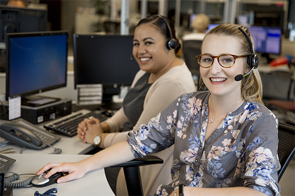 Two women smiling, working at desks with headsets on