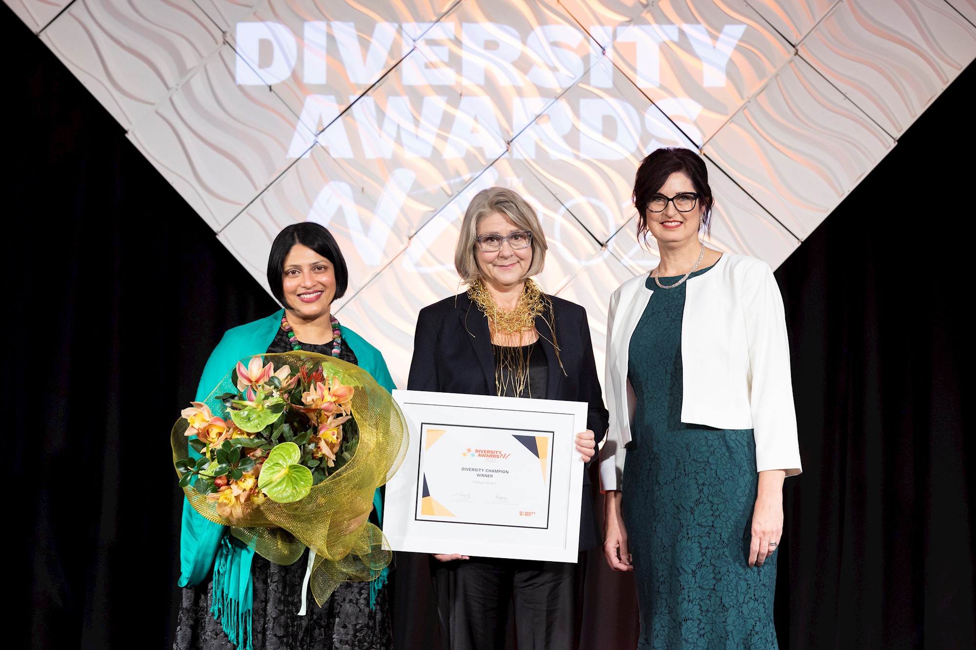 Dellwyn Stuart on stage with Diversity Champion certificate and flowers