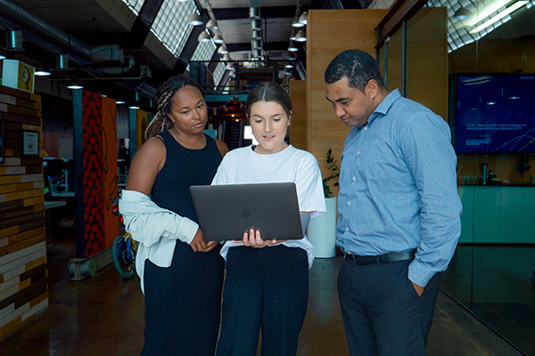 Three people in workplace corridor, analysing computer