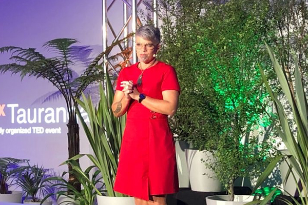 Shelly Davis, speaking on stage surrounded by native greenery