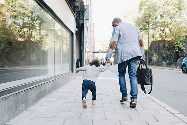 Man and child walking down street, hand in hand