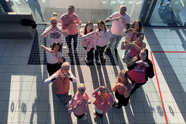 A group of staff wearing pink standing in a love heart shape and making love hearts with their hands